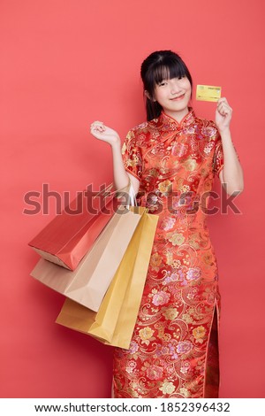 Portrait Cute young Asian woman wear Chinese dress with a shopping bag and credit card for Chinese new year on a red background