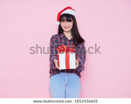Cheerful young girl wearing santa hat giving gift box isolated over pink background