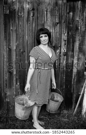 Portrait of a woman standing with buckets in her hands in the village. Black and white photography.