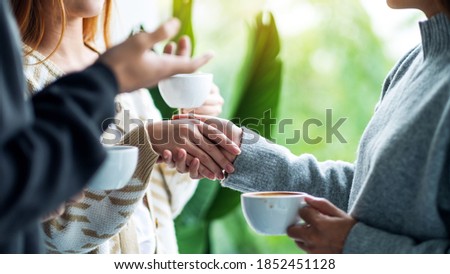 Closeup image of two people holding hands while drinking coffee together