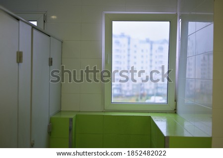 The walls are white and green. Photo of a public bathroom toilet with a door and a window.