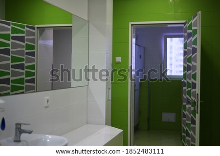 The walls are white and green. Photo of a public bathroom toilet with a door and a window.