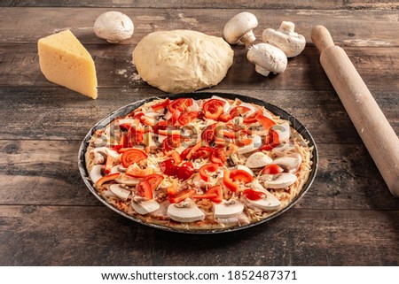 Homemade pizza on wooden background. Raw dough for pizza preparation with ingredient: tomato sauce, mozzarella, tomatoes, basil, olive oil, cheese, spices served on rustic wooden table.