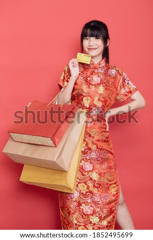 Portrait Cute young Asian woman wear Chinese dress with a shopping bag and credit card for Chinese new year on a red background