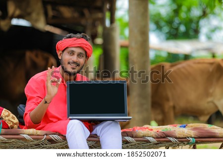 Young indian farmer showing laptop blank screen at home