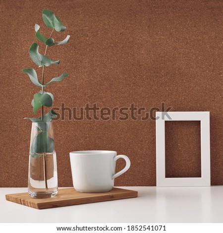 Frame, vase with eucalyptus and cup, cork background. Mock up, copy space. Folk