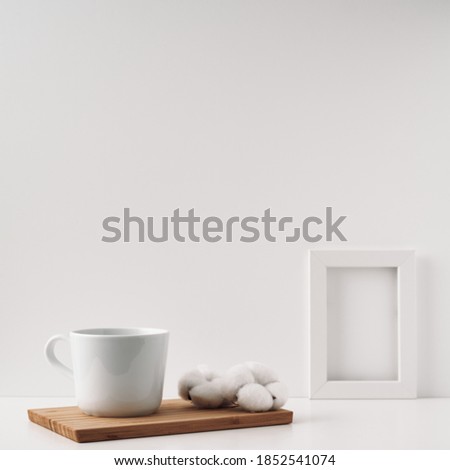 Frame, cotton and a cup on a wooden board, white background. Mock up, copy space. Folk