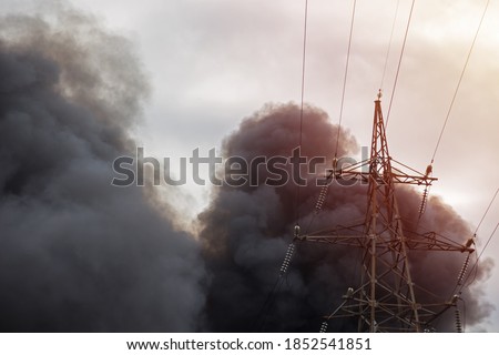 Black smoke from a fire over the city against a cloudy sky with a high-voltage tower Royalty-Free Stock Photo #1852541851