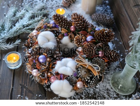 Christmas wreath made of natural materials on a brown wooden background with fir branches, candles and artificial snow.
