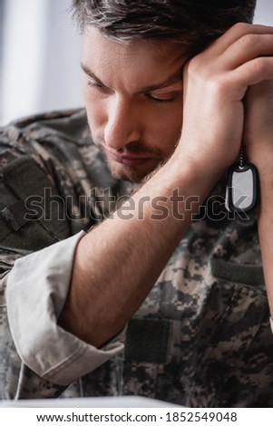 sad soldier in camouflage uniform holding military tag