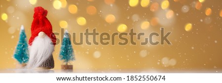 Knitted gnome with tree on gold background with yellow lights and snowflakes