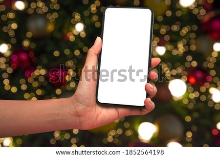 Close up hand holding phone isolated on white background with Illuminated  blurred bokeh of  Christmas tree decoration with  hanging lights ball. Christmas festival background concept.