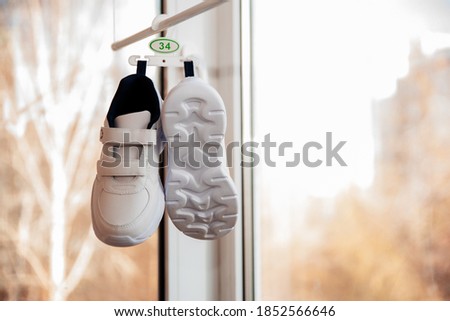 White sneakers size 34 hanging on a hook on the balcony, blurred background