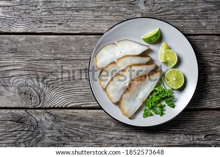 halibut fish slices served with lime on a plate on a rustic wooden table, horizontal view from above, flat lay,  free space
