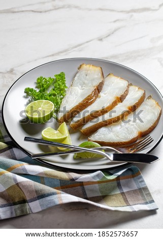 halibut fish slices served with lime on a plate on a marble table, vertical view from above