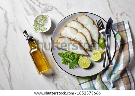 halibut fish slices served with lime on a plate on a marble table, horizontal view from above, flat lay
