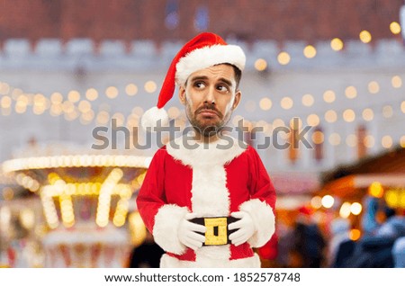 emotion, expression and winter holidays concept - sad man in santa claus costume over christmas market background (funny cartoon style character with big head)