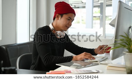 Image of male creative graphic designer is using color selection and working on computer at workplace with work tools and accessories.