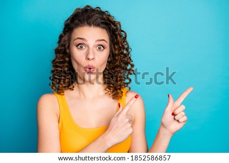 Photo of cute lovely young lady direct fingers empty space excited look amazed wear yellow singlet isolated blue color background