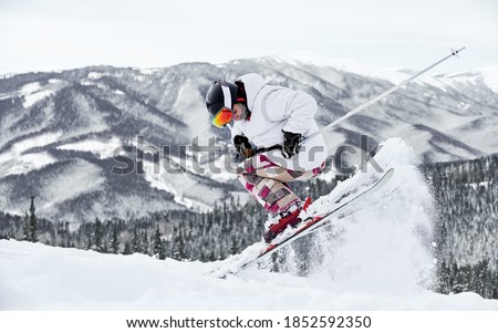 Full length of male skier in jacket and helmet skiing on fresh powder snow with beautiful winter mountains on background. Man freerider making jump while sliding down snow-covered slopes.