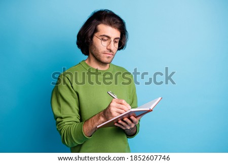 Photo of focused bearded guy hold notepad pen write wear spectacles green pullover isolated blue color background