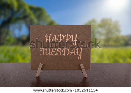 Happy Tuesday card on the table with sunny green forest background.