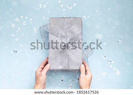 hands holding christmas gift on snowy blue background