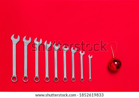 Set of wrenches different size and christmas tree ball toy lays on a red background. Banner with tools and the place for greeting text with industrial new year holiday concept. Close-up.