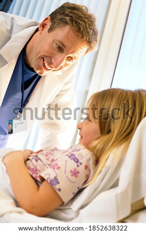 A slant vertical view of a Doctor in white coat smiling at the girl lying on a hospital bed