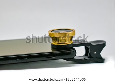 Black smartphone with lens on clip isolated on white. External wide-angle lens and clip are attached to the mobile phone. A modern smartphone with an extra lens. Close-up