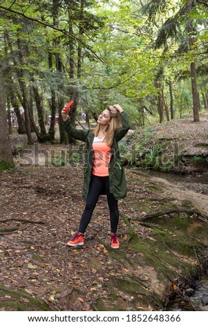 Pretty woman taking pictures while walking in the forest in autumn