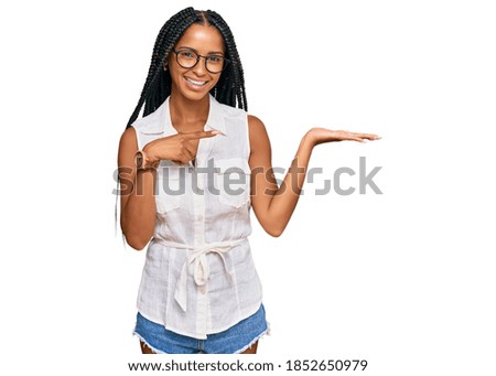 Beautiful hispanic woman wearing casual clothes and glasses amazed and smiling to the camera while presenting with hand and pointing with finger. 