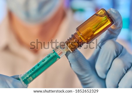 Researcher with face mask fills a syringe with medication. Filling a syringe with vaccine. Vial with vaccine. Biontech Pfizer Novavax Moderna Curevac Astrazeneca. Vaccine candidate. Vaccine syringe. Royalty-Free Stock Photo #1852652329