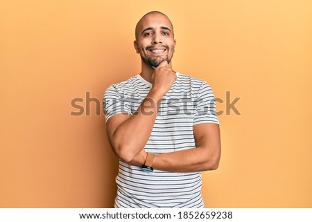 Hispanic adult man wearing casual clothes smiling looking confident at the camera with crossed arms and hand on chin. thinking positive. 