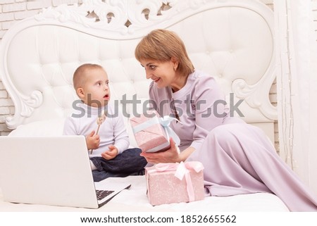 A boy with Down syndrome and a disability sits with his mother on the couch, online video greetings for Merry Christmas and New Year, holidays at home, social distance.
