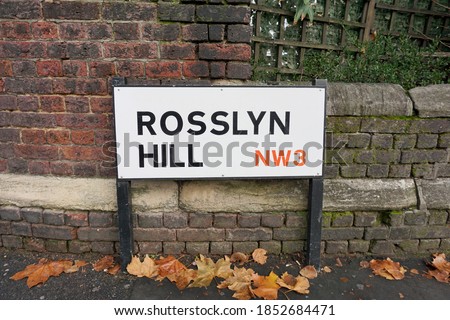Street sign of Rosslyn Hill NW3 in London Borough of Camden, black and red letters on steel white plate in front of old brick wall, London, England, UK