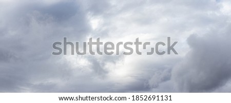 Cloudy sky with gray clouds and a light gap in the center, panorama of the sky