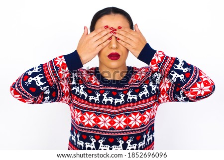 Young beautiful Arab woman wearing Christmas sweater against white wall covering eyes with both hands, doesn't want to see anything or feeling ashamed. Human feelings reactions.