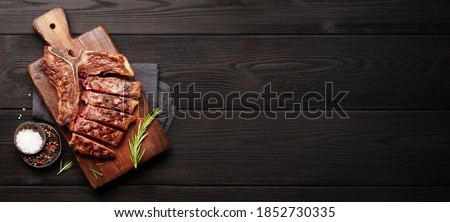 T-bone grilled beef steak with spices and herbs on wide wooden background. Top view flat lay with copy space Royalty-Free Stock Photo #1852730335