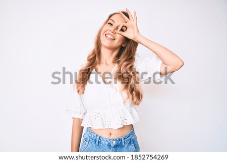 Young caucasian woman with blond hair wearing casual summer clothes smiling happy doing ok sign with hand on eye looking through fingers 