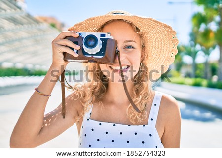 Young beautiful caucasian woman with blond hair smiling happy outdoors on a summer day using vintage camera