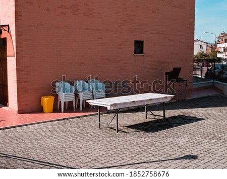 An isolated table in the courtyard with stacked  chairs and a barbecue grill against the wall (Gubbio, Umbria, Italy, Europe)