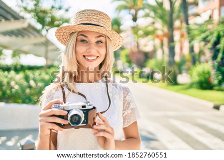 Young caucasian tourist girl smiling happy using vintage camera at street of city.