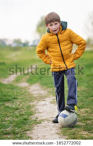 A boy in nature stands with a soccer ball.