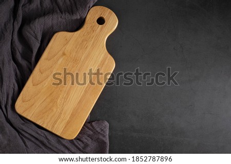Top view above of Wooden chopping board with apron on dark black table background. Empty wood cutting board with handle and hole for hanging with copy space.
