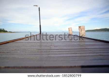 Background picture of a dark brown wooden bridge extending into the sea. There is a blurred background of the sky and the sea. Focus on the middle of the bridge.