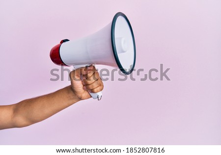 Hand of hispanic man holding megaphone over isolated pink background.