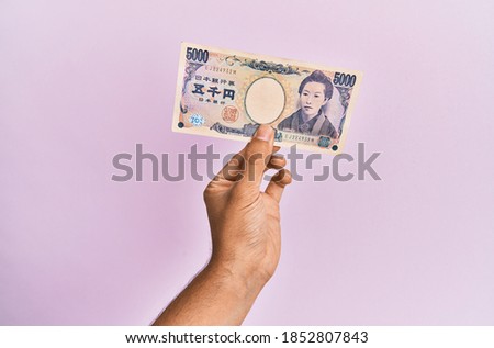 Hispanic hand holding one 5000 japanese yen banknote over isolated pink background.