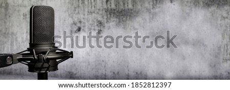 Professional microphone on concrete wall background, urban audio recording banner with copy space, broadcasting or podcasting backdrop