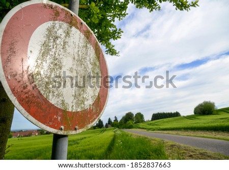 Stop sign in front of a paved path through green fields and meadows in a rural and car-free area with blurred background - selective focus